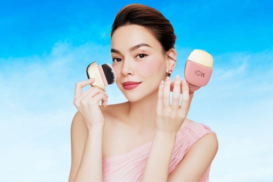 Người phụ nữ cầm cọ trang điểm và thiết bị làm đẹp, nền trời xanh.