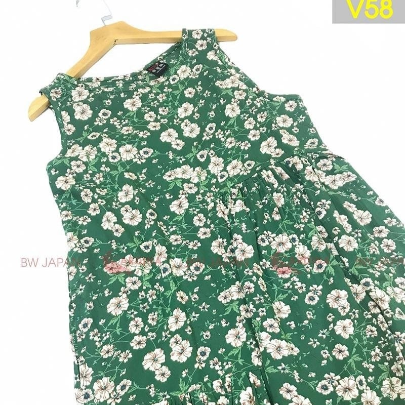Váy xanh lá họa tiết hoa trắng, không tay, treo trên móc gỗ.