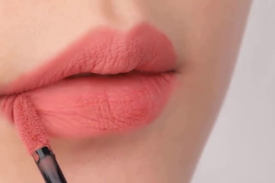 Người đang thoa son môi màu hồng nhạt bằng cọ, tập trung vào đôi môi.