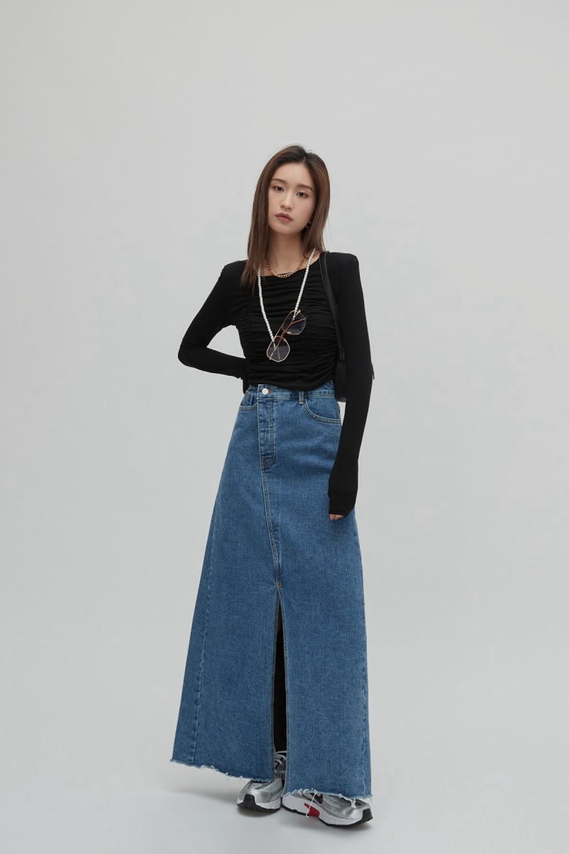 Người mẫu mặc áo đen dài tay, váy denim dài và giày thể thao, đeo dây chuyền và kính mát.