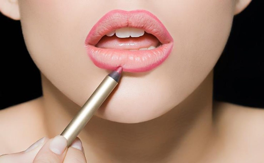 Một người đang dùng bút kẻ viền môi màu hồng để trang điểm cho đôi môi.