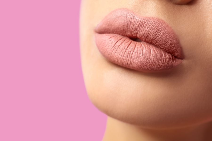 Đôi môi được trang điểm màu hồng nhạt trên nền hồng.