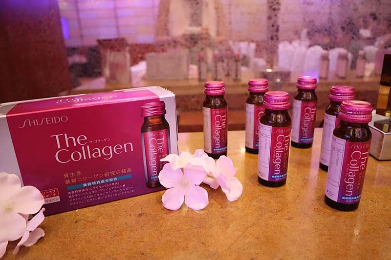 Hộp và chai nước uống collagen trên bàn, có hoa trắng trang trí cạnh bên.