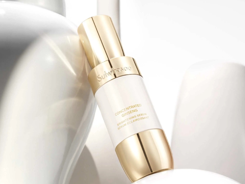 Chai serum màu trắng và vàng đặt trên bề mặt sáng bóng, với chữ in nổi bật trên thân chai.