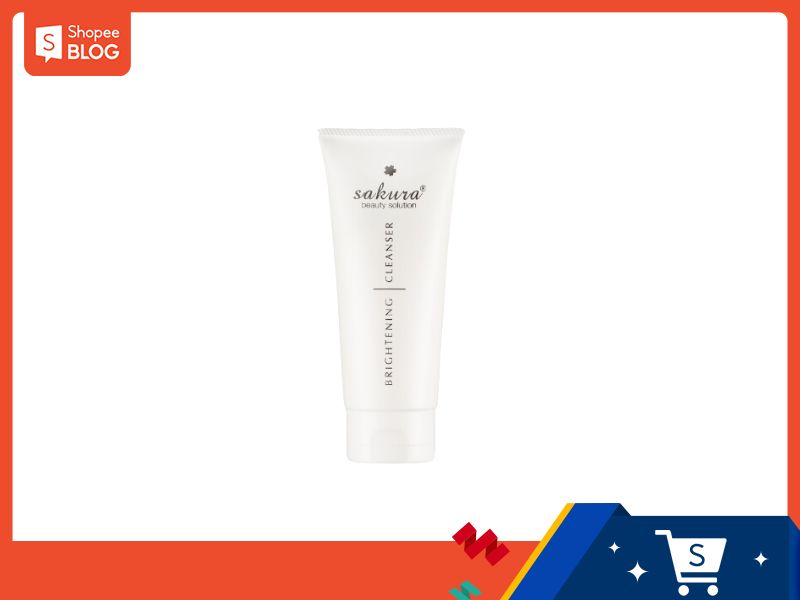 Tuýp kem làm sạch da màu trắng, có chữ "sakura" và "brightening cleanser" in trên thân. Nền trắng cam.
