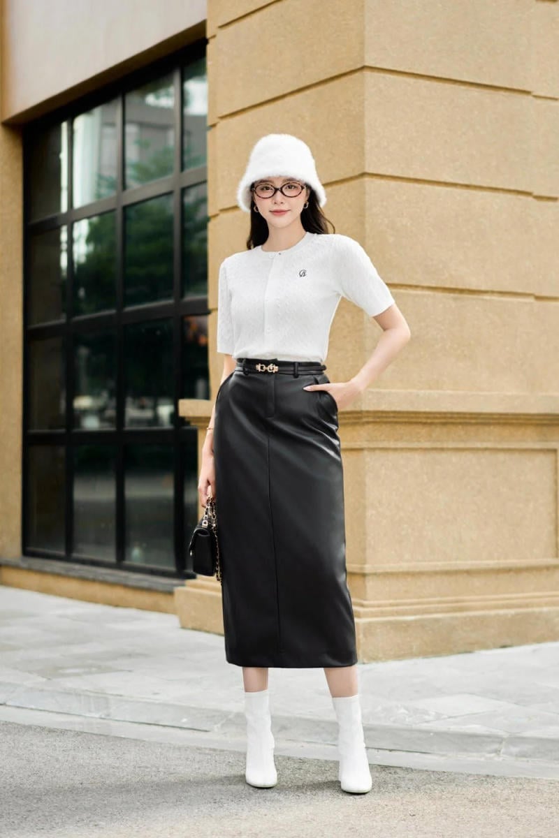 Người mặc áo trắng, váy đen, đội mũ trắng, đứng trước tòa nhà có cửa kính lớn.
