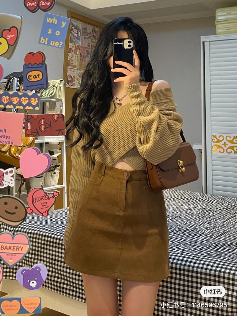 Người chụp selfie trước gương, mặc áo len và váy nâu, xung quanh có nhiều sticker màu sắc.
