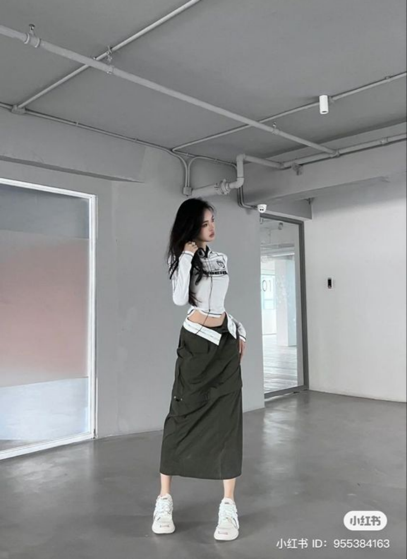 Người mẫu trong trang phục thời trang hiện đại, đứng trong không gian nội thất tối giản với tường xám.