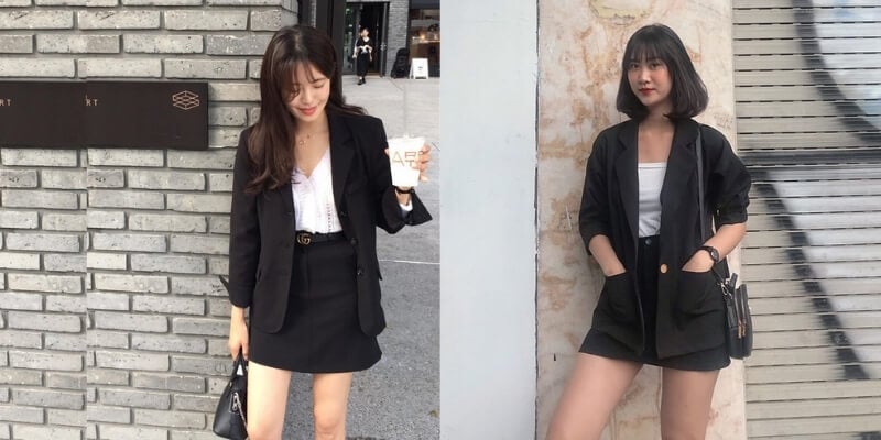 Hai người phụ nữ mặc trang phục màu đen đứng trước tường gạch và cửa cuốn.