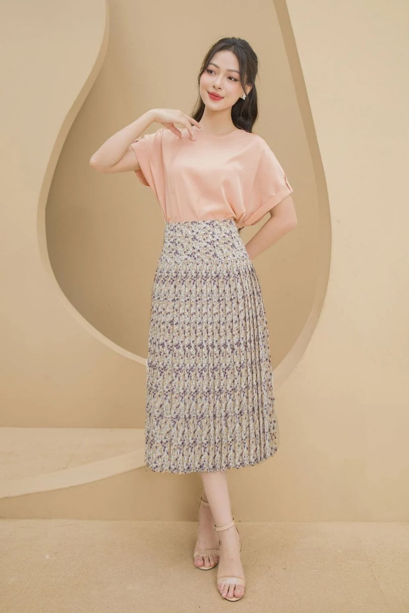 10 Cách Phối Đồ Với Chân Váy Hoa Nhí Giúp Bạn Tỏa Sáng Mùa Hè 13 Người phụ nữ mặc áo hồng và váy hoa đứng trước bức tường màu be.