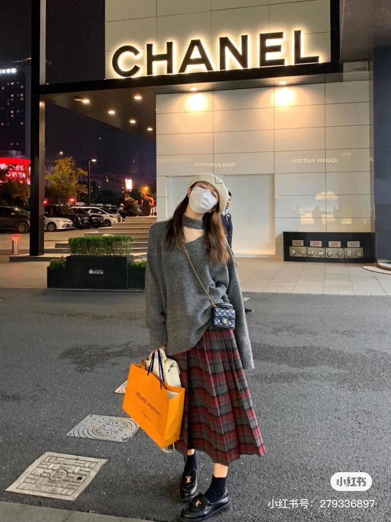 Người đứng trước cửa hàng Chanel, mặc trang phục thời trang và cầm túi mua sắm.