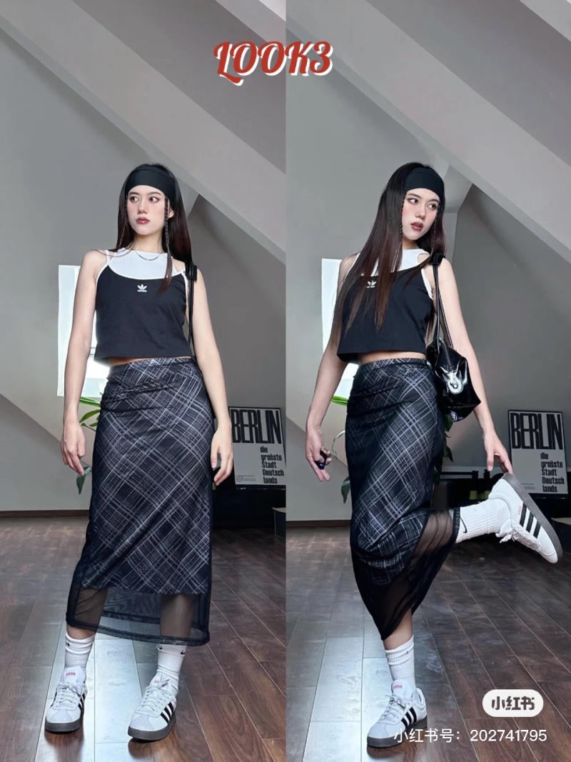 Người mẫu mặc áo crop top đen, váy kẻ sọc, đi giày thể thao, tạo dáng trong phòng có sàn gỗ.