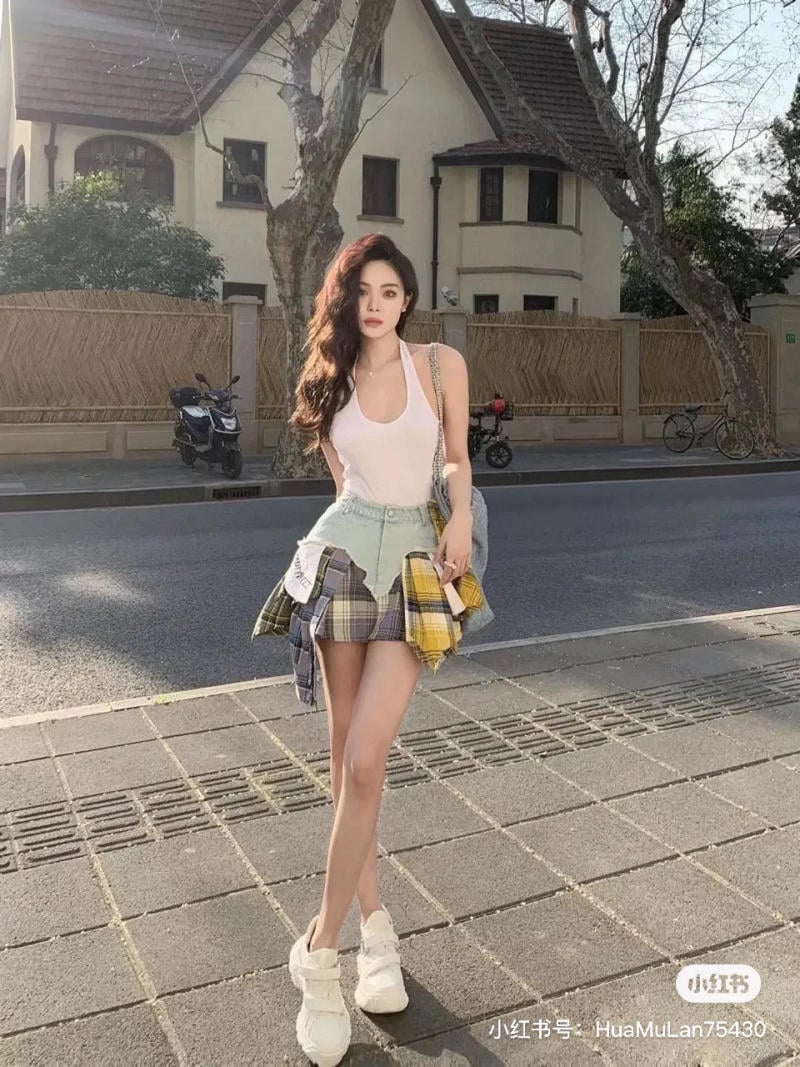 Người mẫu đứng trên vỉa hè, phía sau là ngôi nhà và cây cối, mặc trang phục thời trang sáng màu.