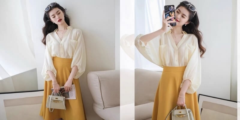 Người phụ nữ mặc áo trắng và chân váy vàng chụp ảnh tự sướng trong phòng sáng, cầm túi xách nhỏ màu xám.