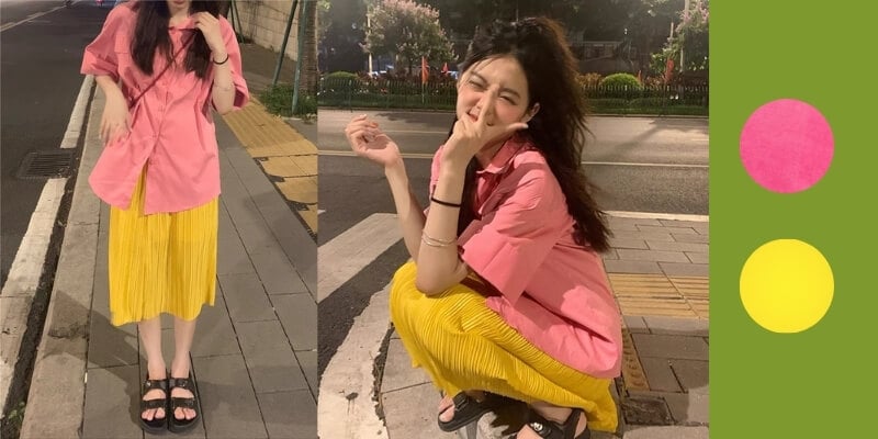 Người mặc áo hồng, váy vàng đứng và ngồi trên vỉa hè vào ban đêm, bên cạnh là hai vòng tròn màu sắc.