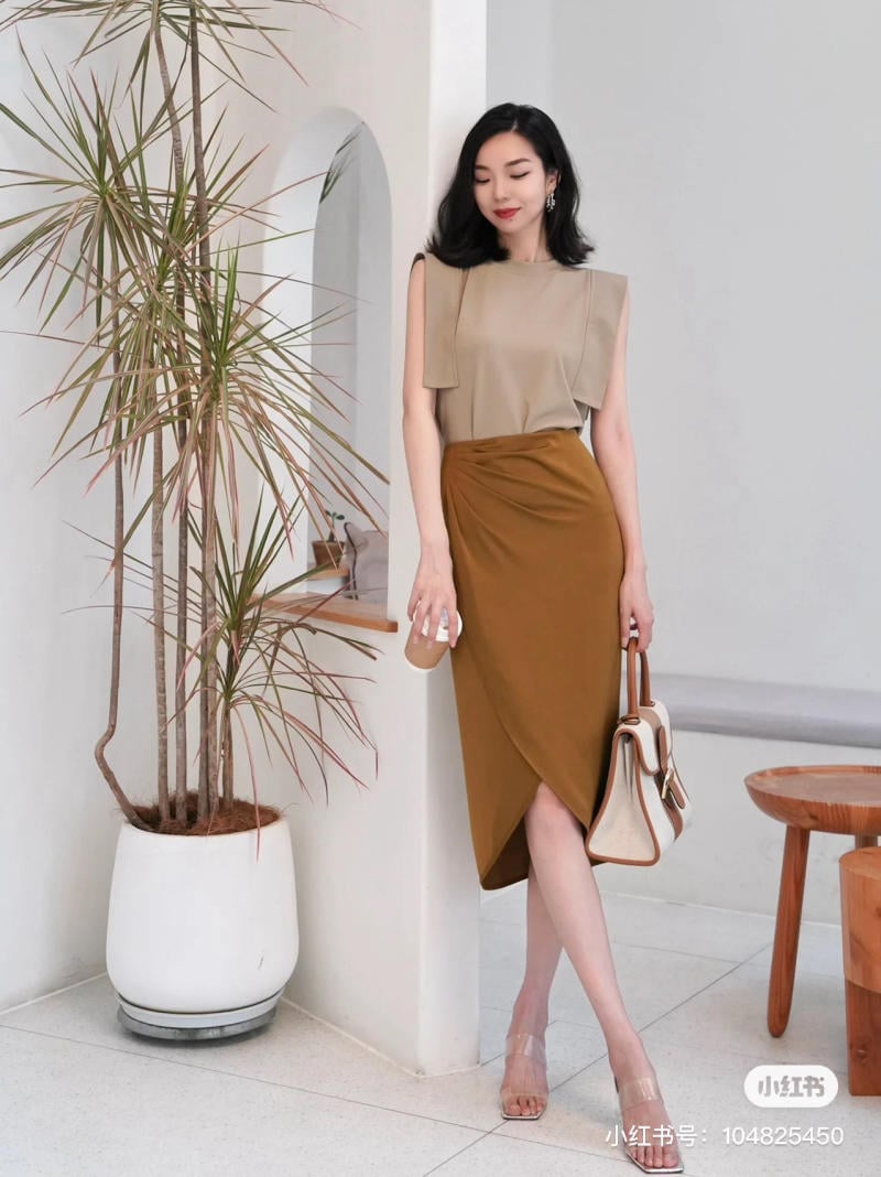 Người phụ nữ mặc trang phục thanh lịch đứng cạnh chậu cây trong không gian nội thất hiện đại.