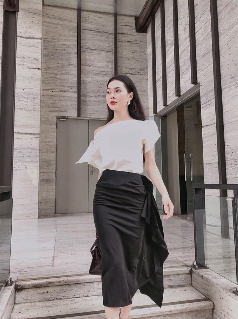 Người phụ nữ mặc áo trắng và chân váy đen, đi bộ trong một không gian nội thất hiện đại.