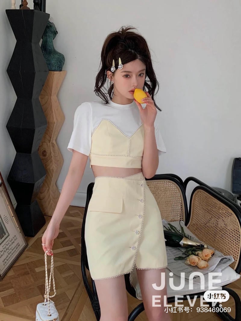 Người phụ nữ mặc trang phục màu vàng nhạt, đứng trong phòng, cầm một quả đào gần miệng.