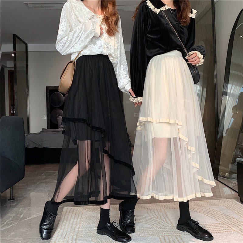 Hai người mặc áo dài tay và váy lưới, một đen một trắng, đứng trong phòng khách hiện đại.