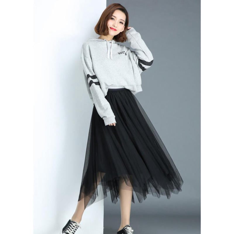 Người mẫu mặc áo hoodie xám và váy đen dài, đứng tạo dáng trên nền xám.