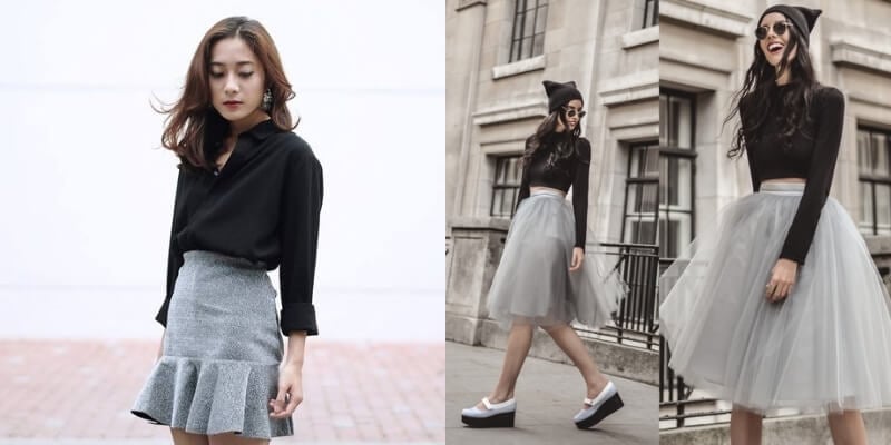 Người mẫu nữ mặc áo đen và váy xám đứng ngoài trời, phông nền tòa nhà và đường phố.