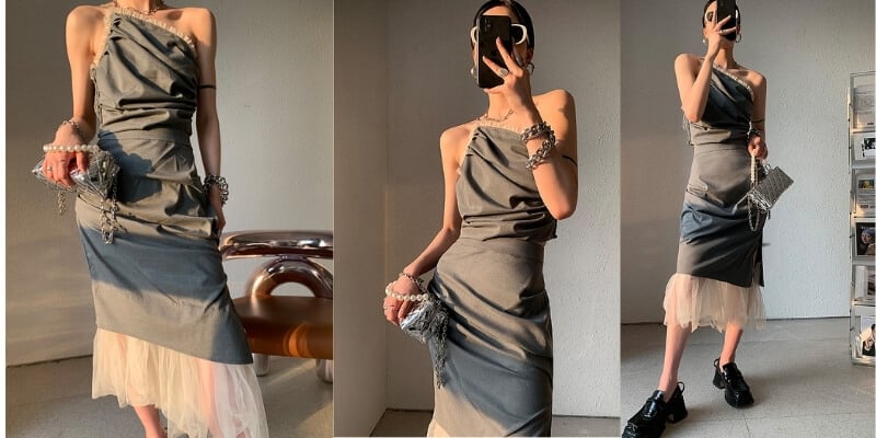 Người mẫu mặc váy xám lệch vai, kết hợp phụ kiện, tạo dáng trong không gian hiện đại, ánh sáng tự nhiên chiếu vào.