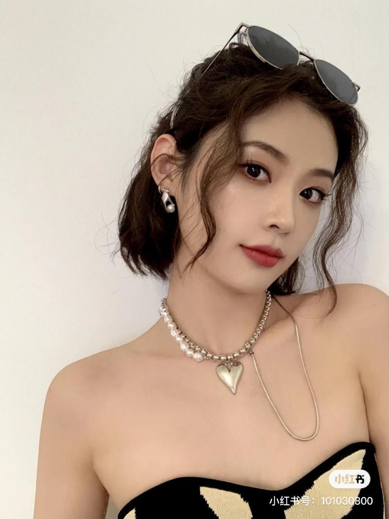 Người phụ nữ đeo kính râm trên đầu, trang điểm nhẹ, diện vòng cổ và mặc áo trễ vai.