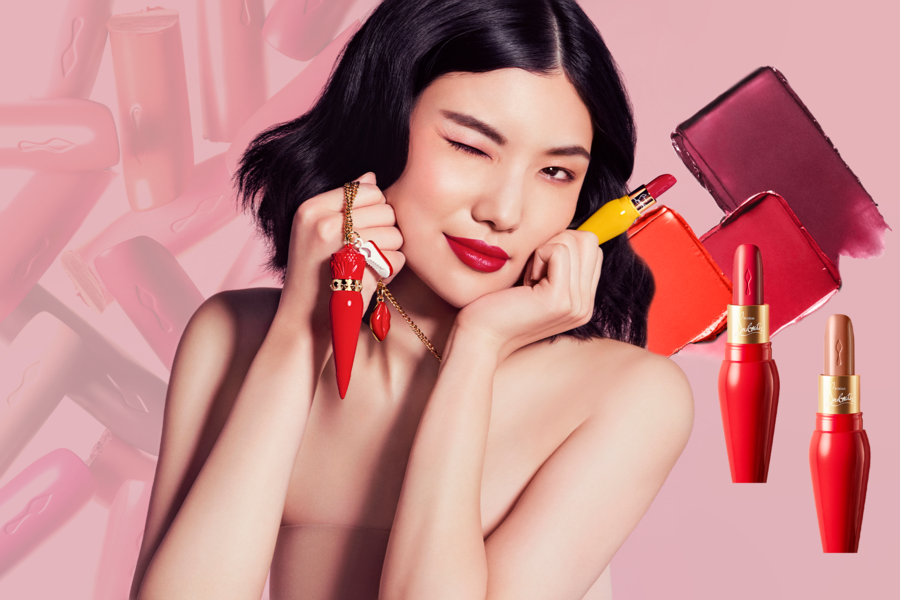 Người mẫu cầm son môi đỏ, nền hồng, có nhiều thỏi son và mẫu màu son khác nhau.