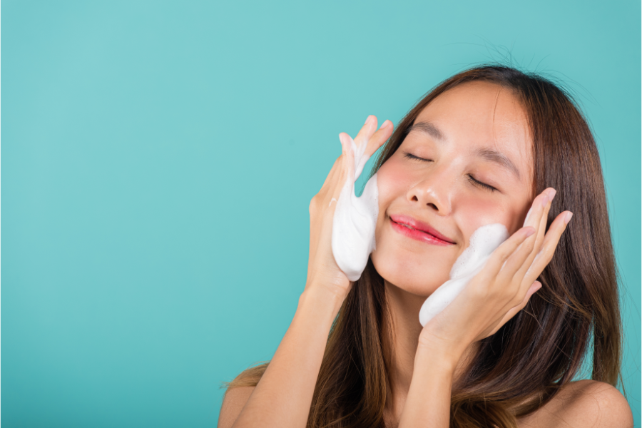 Người phụ nữ đang rửa mặt bằng bọt xà phòng trên nền xanh dương.