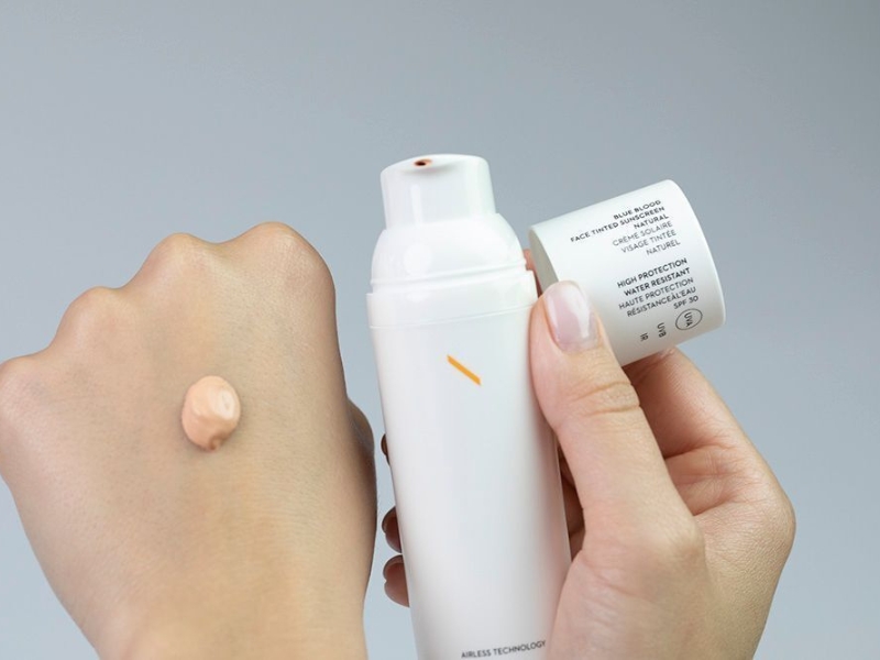 Người cầm chai kem dưỡng da, một ít kem được bơm ra và bôi thử trên mu bàn tay.