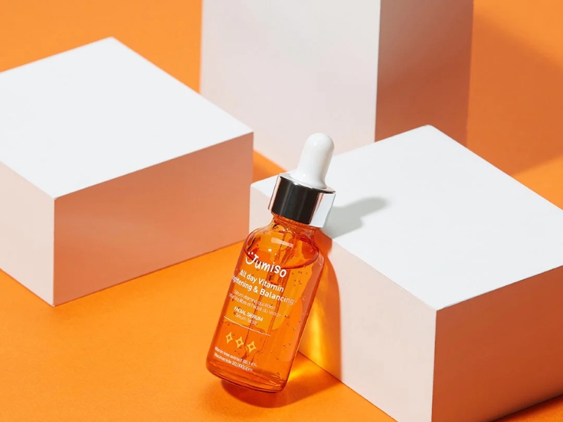 Chai serum màu cam với ống nhỏ giọt, đặt trên nền cam và các khối hộp trắng.