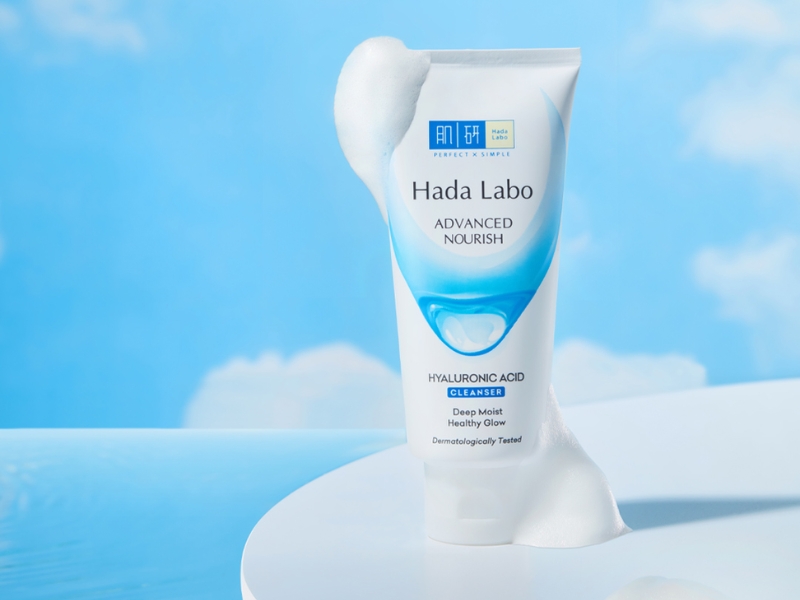 d98c6b08-sua-rua-mat-cho-da-kho-nhay-cam-26 Tuýp sữa rửa mặt Hada Labo Advanced Nourish trên nền xanh, có bọt trắng xung quanh.