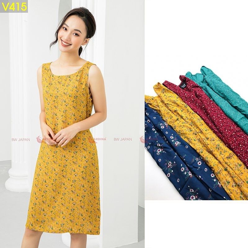 Người mẫu mặc váy hoa vàng, bên cạnh là nhiều mẫu váy khác màu sắc khác nhau được xếp chồng lên nhau.