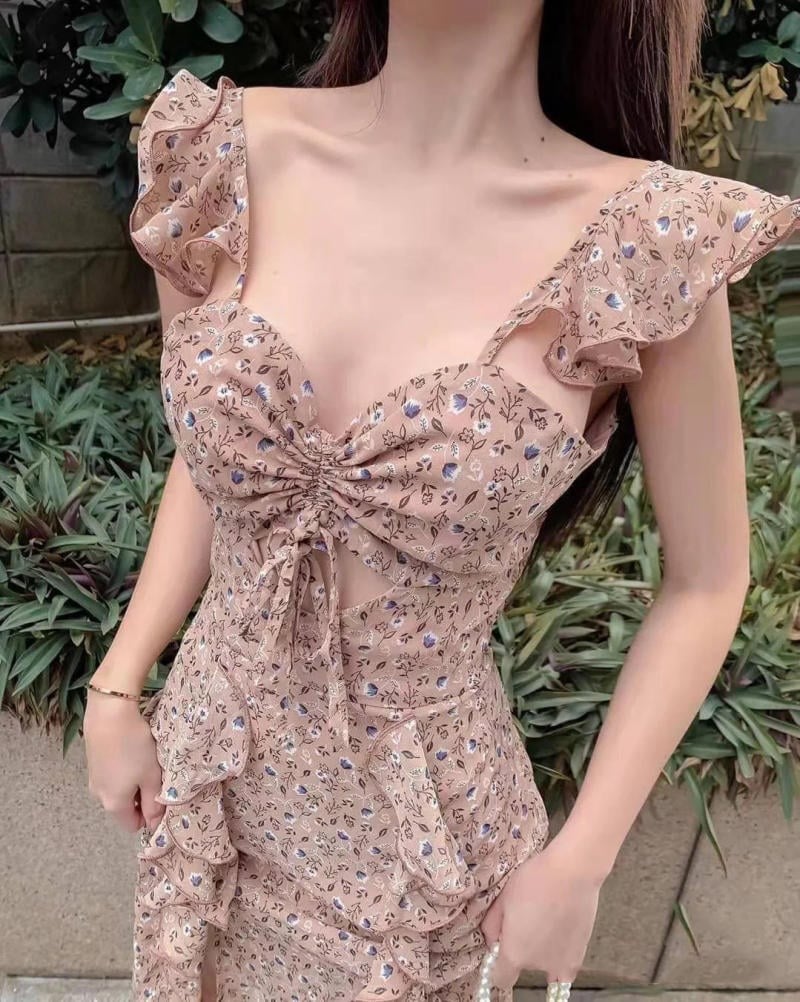 Người mặc váy hoa màu nâu nhạt với thiết kế xếp nếp và chi tiết buộc dây, nền là cây xanh.