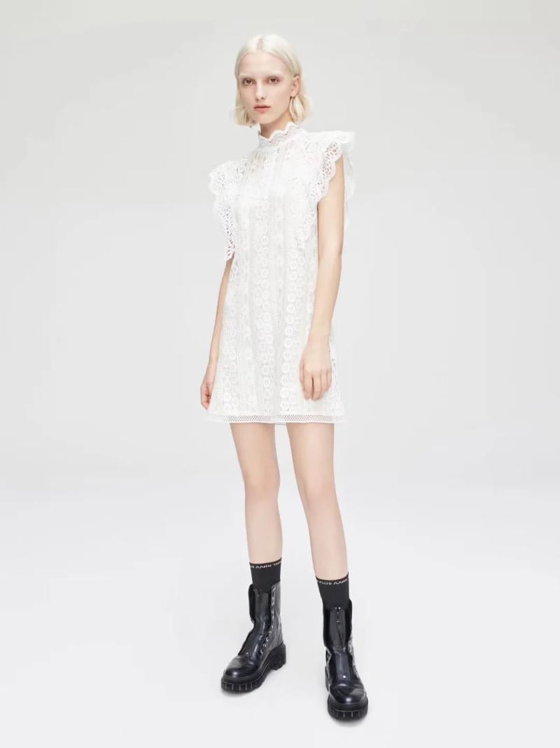Người mẫu mặc váy trắng ren ngắn và giày boots đen đứng trên nền trắng.