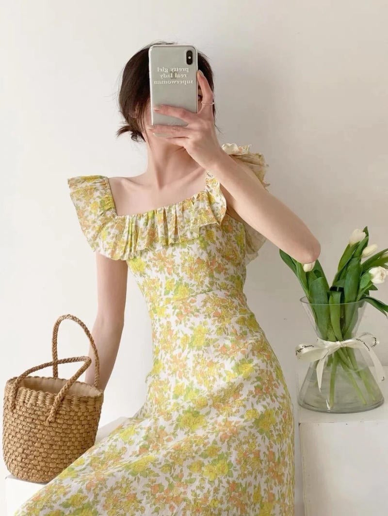 Người mặc váy hoa cầm điện thoại che mặt, bên cạnh có giỏ mây và bình hoa tulip trắng.
