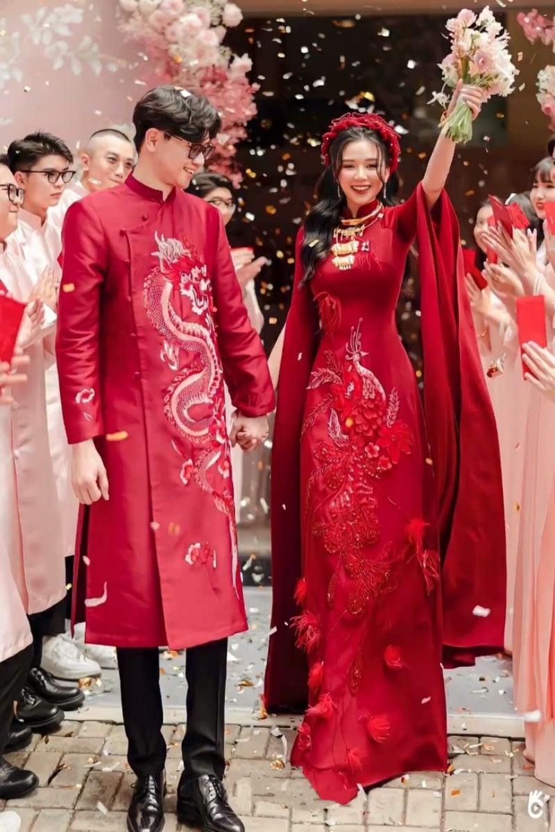 Cô dâu chú rể mặc trang phục truyền thống màu đỏ, vui vẻ giữa vòng tay chúc mừng của bạn bè trong lễ cưới.