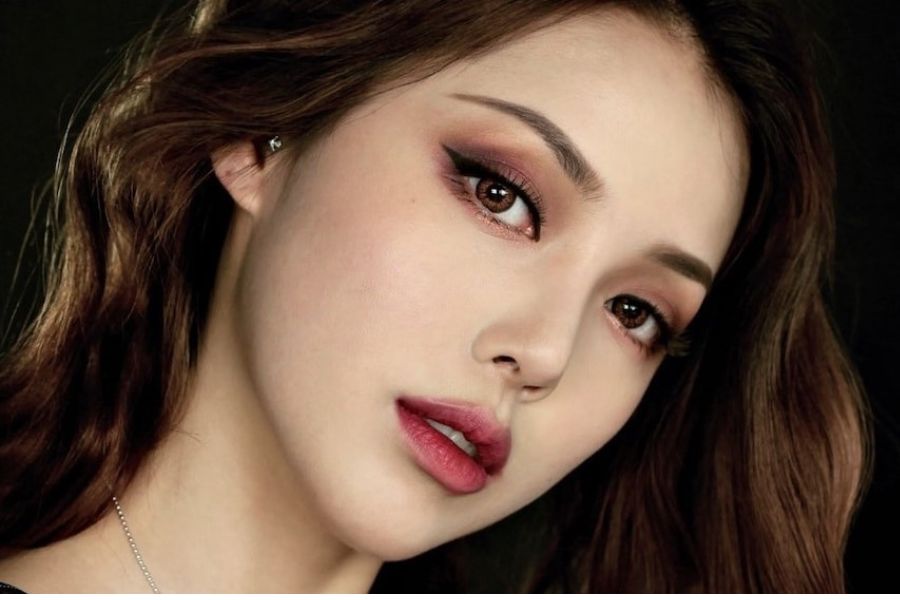 Cận cảnh khuôn mặt người với trang điểm mắt đậm, ánh sáng dịu nhẹ, tóc nâu gợn sóng.