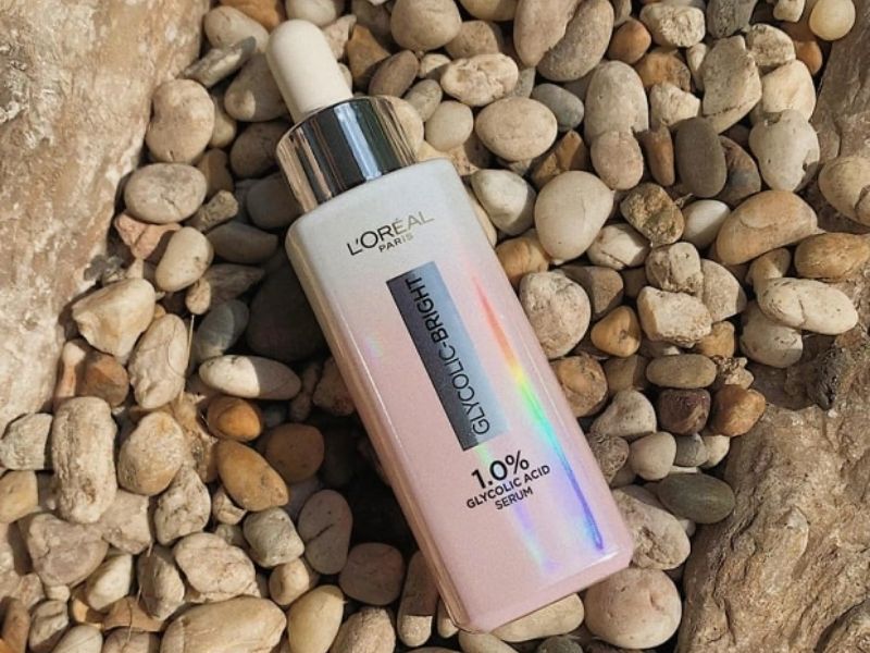 dd28691e-serum-lam-deu-mau-da-15 Chai serum đặt trên nền sỏi đá, với nhãn hiệu và thành phần trên thân chai.