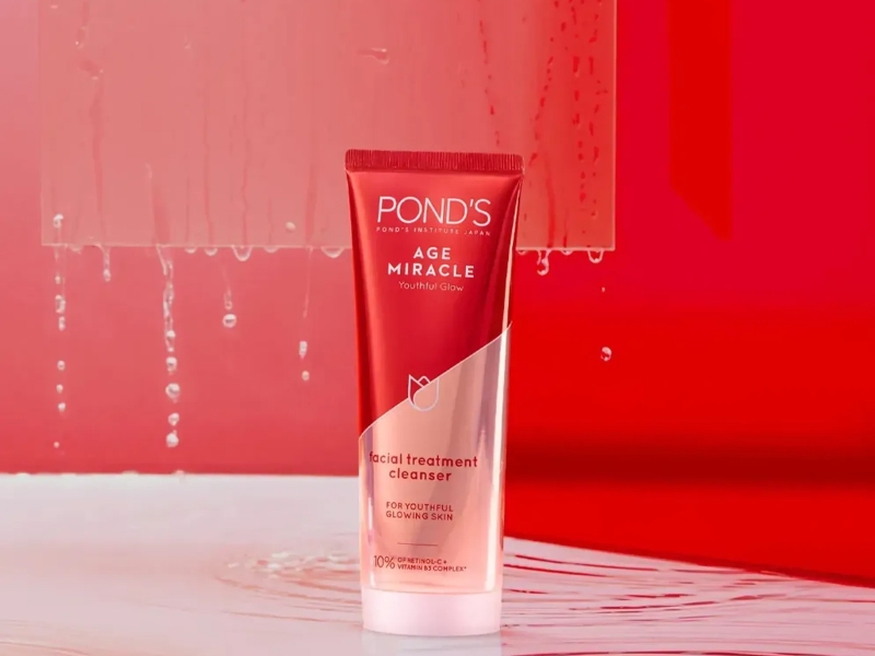 e2f05a1a-sua-rua-mat-chong-lao-hoa-2 Tuýp sữa rửa mặt Pond's Age Miracle trên nền đỏ, với các giọt nước rơi phía sau.