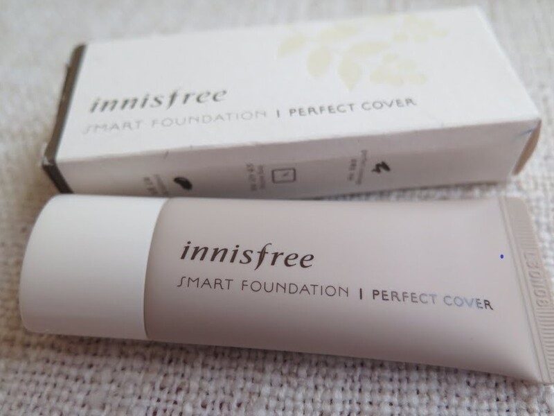 e3234627-1-1 Tuýp kem nền Innisfree Smart Foundation Perfect Cover bên cạnh hộp giấy trên nền vải.