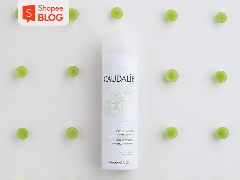 Chai nước xịt dưỡng da Caudalie và các lát nho xanh xếp đều trên nền trắng.