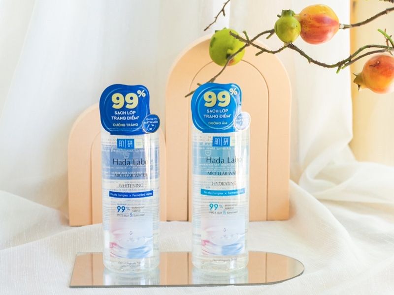 ff191679-nuoc-tay-trang-tot-nhat-hien-nay-23 Hai chai nước tẩy trang đặt trên gương, nền trắng và trang trí với cành cây có quả.