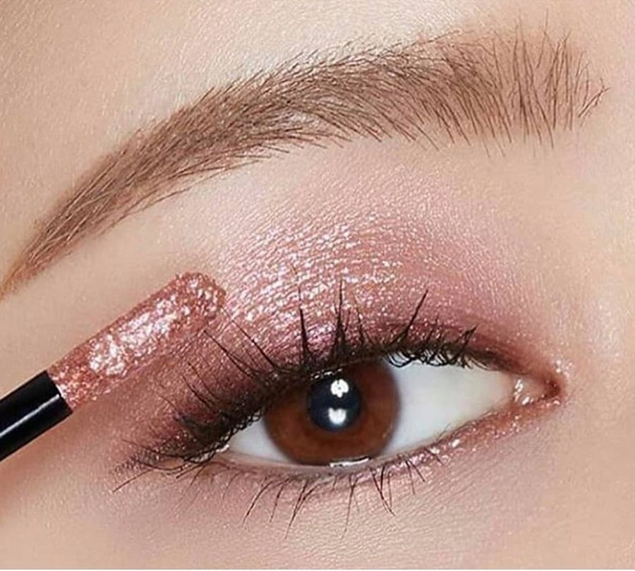 Cận cảnh mắt với lớp phấn mắt nhũ hồng và cọ trang điểm, lông mi dài và cong.