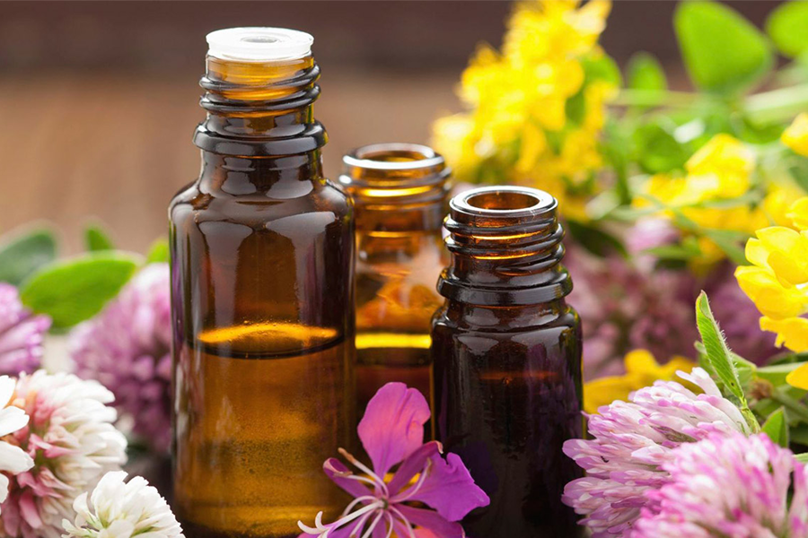 Ba chai thủy tinh nâu chứa dầu, đặt giữa các loại hoa màu sắc tươi sáng.