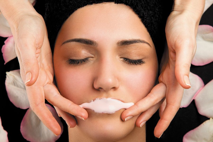 Người đang được chăm sóc da mặt với mặt nạ trên môi, xung quanh là cánh hoa hồng.