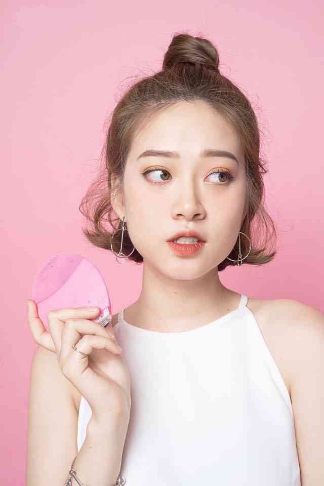 may-luna Người phụ nữ cầm thiết bị chăm sóc da màu hồng, nền màu hồng, mặc áo trắng.