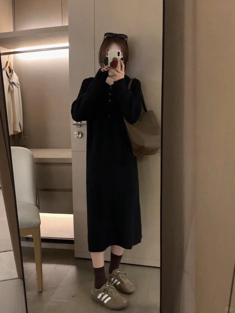 Người chụp ảnh tự sướng trong gương, mặc váy đen dài, đi giày thể thao, tay cầm điện thoại di động.