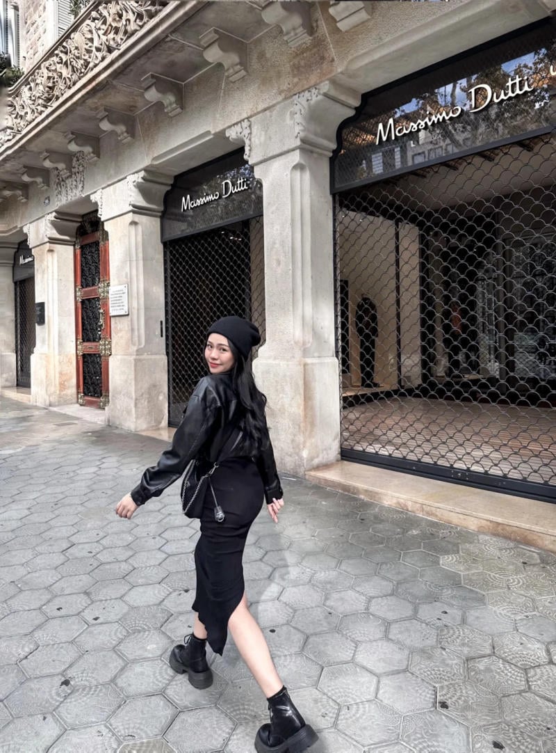 Người phụ nữ mặc đồ đen đi trên vỉa hè, phía trước cửa hàng thời trang với cửa cuốn đóng kín.
