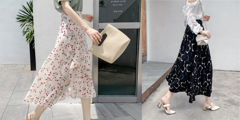 Hai người mặc váy dài, một người váy hoa trắng, một người váy đen họa tiết, đang đi bộ trên vỉa hè.